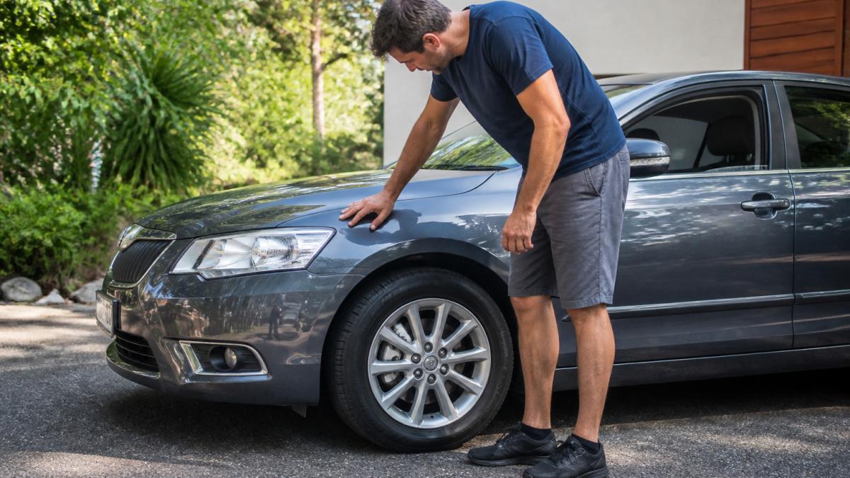 Driver pressing on the car bonnet to test the front shock absorbers during a DIY suspension repair check.