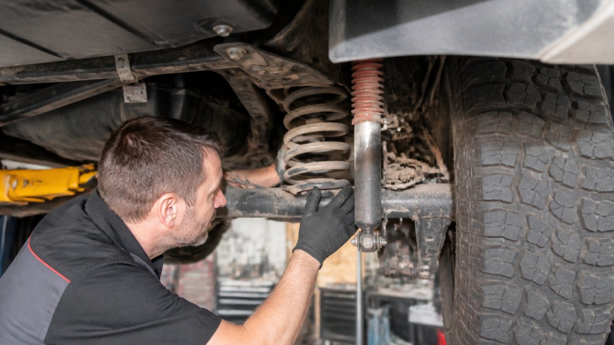 Professional mechanic inspecting caravan suspension components including shock absorber and spring assembly during off-road capability assessment, hands-on inspection in workshop setting