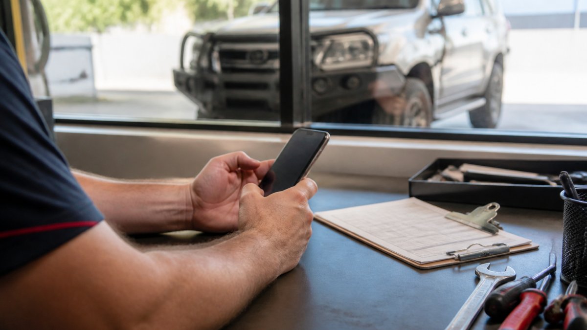 Person using a smartphone to book car safety inspection online with a vehicle in the background